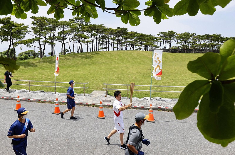 A torch relay runner carries the Olympic torch Saturday near Nago, Japan. A leg of the relay on Okinawa’s resort island of Miyakojima set for today has been canceled with covid-19 cases surging in Japan.
(AP/Hiroki Yamauchi)