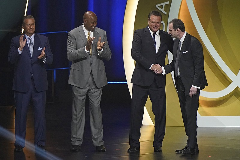 Sean Sutton, right, son of Eddie Sutton, shakes hands with Kansas coach Bill Self, as Kentucky coach John Calipari, left, and Sidney Moncrief after his father was enshrined as part of the 2020 Basketball Hall of Fame class, Saturday, May 15, 2021, in Uncasville, Conn. Moncrief played at Arkansas while Eddie Sutton coached there. (AP Photo/Kathy Willens)
