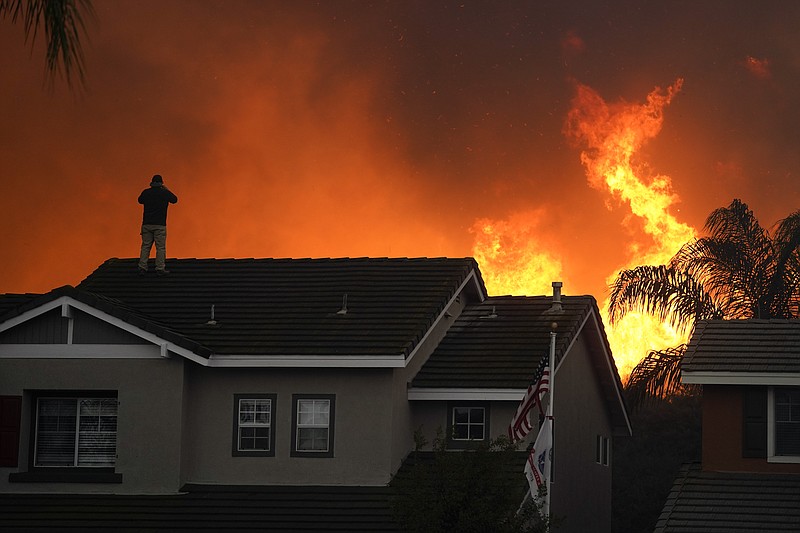 FILE - In this Oct. 27, 2020, file photo, Herman Termeer, 54, stands on the roof of his home as the Blue Ridge Fire burns along the hillside in Chino Hills, Calif. Scientists say the outlook for the western U.S. fire season is grim because it’s starting far drier than 2020’s record-breaking fire year.