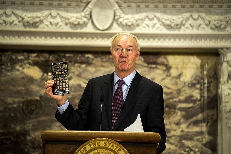 Governor Hutchinson holds up a scratch lottery ticket as he announces a new initiative that will give a lottery ticket or a Arkansas Game and Fish voucher for a fishing and/or hunting license to any Arkansan who gets vaccinated during a weekly address on Arkansas’ response to COVID-19 on Tuesday, May 25. (Arkansas Democrat-Gazette/Stephen Swofford)