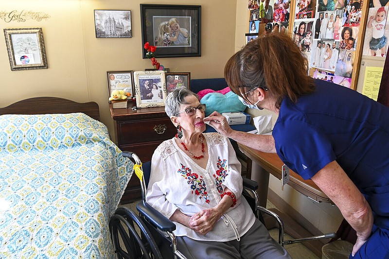 Cheri Place-Chafin (right), director of nursing at Arbor Springs Health and Rehabilitation Center in Opelika, Ala., helps resident Eleanor Garrison with her lipstick in this Feb. 3, 2021, file photo. Alabama was one of five states — including Arkansas, North Dakota, South Carolina and Tennessee — where at least 95% of local nursing homes saw “long-duration” outbreaks during the covid-19 pandemic, according to a Government Accountability Office analysis. (AP/Julie Bennett)