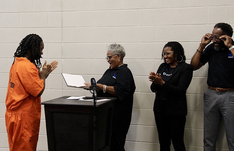 Marlo Carter receives his graduation certificate Thursday from Exodus peer specialist and classroom instructor Marguerite Taggart while receiving applause from Executive Director Myra Woolfolk and peer specialist Raynard White. 
(Pine Bluff Commercial/Eplunus Colvin)