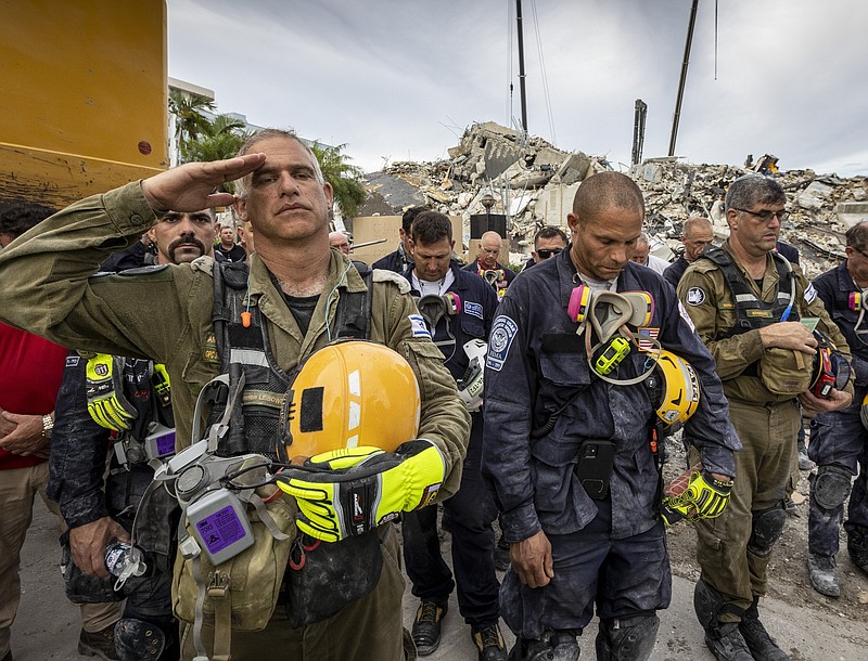 A member of the Israeli search and rescue team, left, salutes in front of the rubble that once was Champlain Towers South during a prayer ceremony, Wednesday, July 7, 2021, in Surfside, Fla. Members of search and rescue teams and Miami-Dade Fire rescue, along with police and workers who have been working at the site of the collapse gathered for a moment of prayer and silence next to the collapsed tower. (Jose A Iglesias/Miami Herald via AP)