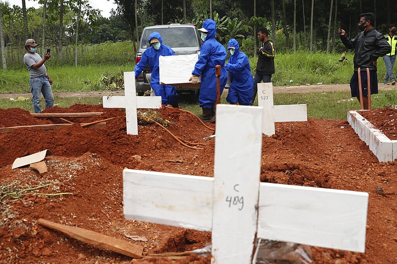 Workers in protective suits carry a coffin containing the body of a covid-19 victim to a grave for a burial at Cipenjo cemetery in Bogor, West Java, Indonesia, on Wednesday, July 14, 2021. The world's fourth most populous country has been hit hard by an explosion of covid-19 cases that have strained hospitals on the main island of Java. (AP/Achmad Ibrahim)