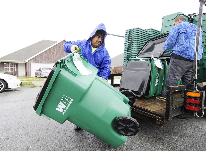 Anthony Rodriguez, left, with Rehrig Pacific Company, carries a new Waste Management cart to a home in Springdale, Monday, May 10, 2010. (NWA Democrat-Gazette, File)