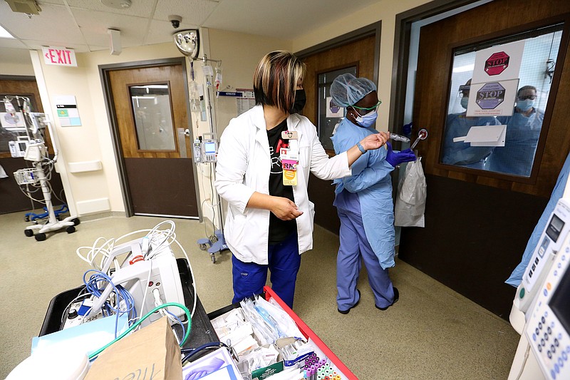 Nurses Kia Kandlbinder (left) and Brionna Rivers hand equipment through the door to fellow nurses in one of the Covid wards at University of Arkansas for Medical Science on Thursday, July 22, 2021, in Little Rock. .(Arkansas Democrat-Gazette/Thomas Metthe)