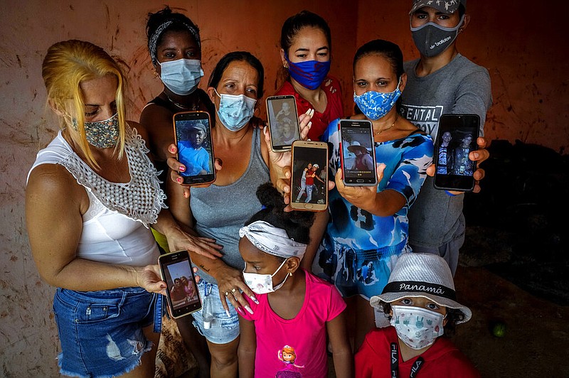 Zuleydis "Zuly" Elledias (left) shows a cellphone photo of her missing husband to a child while her neighbors pose for a group picture holding up cellphone photos of their missing relatives in Orlando Nodarse, about 38 miles west of Havana, Cuba, in this June 30, 2021, file photo. Each of the photographed relatives ventured out in homemade boats in an attempt to reach Florida. Cuba is seeing a surge in unauthorized migration to the United States, fueled by an economic crisis. (AP/Ramon Espinosa)