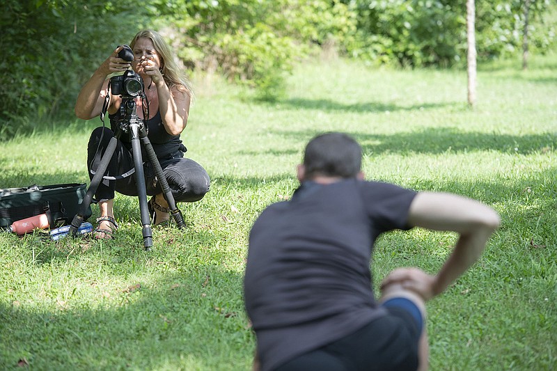 Diana Michelle of Fayetteville sets up her camera to record Paul Summerlin of Fayetteville while he performs some yoga poses Wednesday July 28, 2021 at Wilson Park in Fayetteville. (NWA Democrat-Gazette/J.T. Wampler)