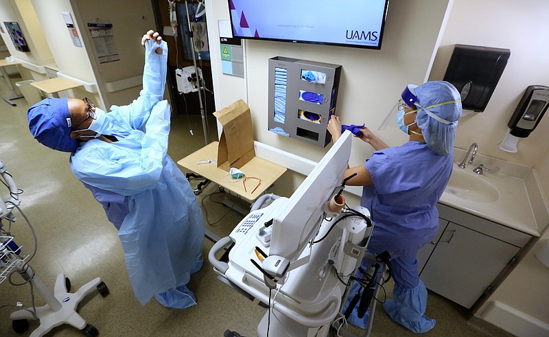 Nurse Takela Gardner (left) puts on personal protective equipment, or PPE, before entering a room in one of the covid wards at University of Arkansas for Medical Sciences in Little Rock in this July 22, 2021, file photo. (Arkansas Democrat-Gazette/Thomas Metthe)