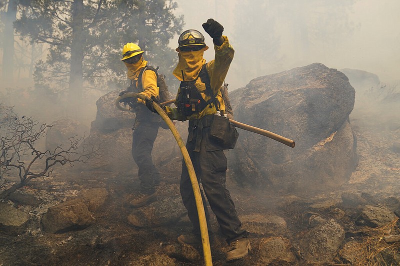 Two firefighters carry a water hose up a hill to extinguish a backfire set to prevent the Caldor Fire from spreading near South Lake Tahoe, Calif., on Thursday, Sept. 2, 2021. (AP/Jae C. Hong)