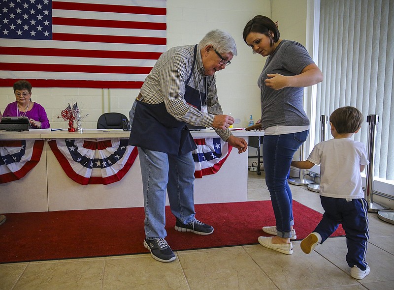 Election official Larry Rountree (left) moves in with an "I voted" sticker but Lawson Verde, 3, retreats behind his mother Stephanie Lawson as she prepares to early vote in a Bryant School special election in this March 2017 file photo. (Arkansas Democrat-Gazette/Stephen B. Thornton)