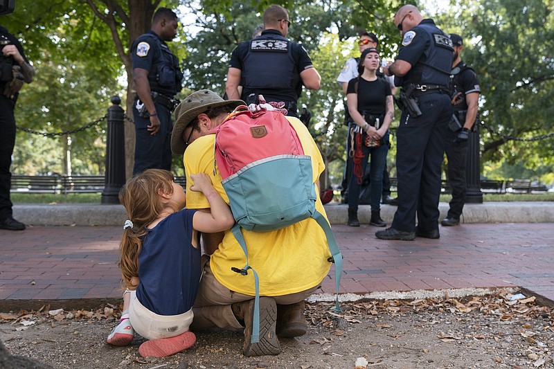 A 4-year-old looks up at her father as a family friend is questioned by police after members of the protest group Extinction Rebellion climbed a wall at the U.S. Chamber of Commerce in Washington during a climate protest Thursday. The economic risks of climate change were outlined in a 40-page report released by the Biden administration Friday.
(AP/Jacquelyn Martin)