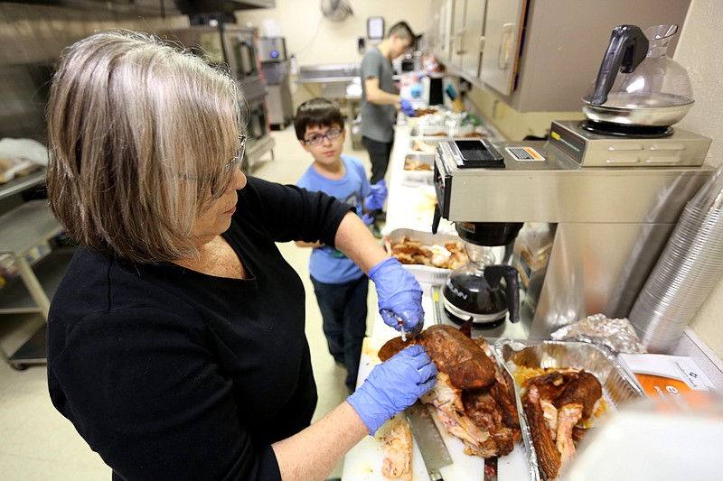 Volunteers Diane Gaynor (from left), her grandson Caden Herrera, 9, and volunteer Jaren Garcia, slice smoked turkeys for the Salvation Army Thanksgiving meal at Genesis Church in Fayetteville in 2019. With covid-19 rates down and vaccines readily available, more churches than last year are holding Thanksgiving worship services and meals.
(NWA Democrat-Gazette/David Gottschalk)