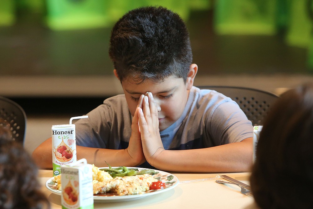 Orestes Cortez joins other participants in the LifeSource International Kids Life Camp in saying grace before eating a meal in Fayetteville in 2017.
(NWA Democrat-Gazette file photo)