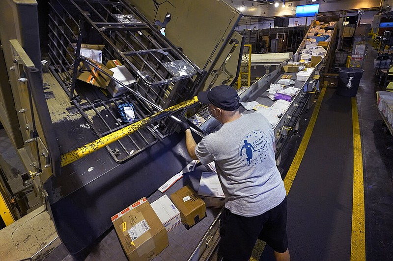 Derek Baszkiewicz frees a stuck package as parcels jam a conveyor belt at the United States Postal Service sorting and processing facility in Boston in this Nov. 18, 2021, file photo. On the busiest days, about 170,000 packages are processed at the facility. (AP/Charles Krupa)