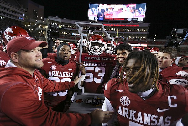 Arkansas defensive coordinator Barry Odom (left) helps players carry the Battle Line Trophy after the Razorbacks defeated Missouri 34-17 on Friday, Nov. 26, 2021, in Fayetteville.