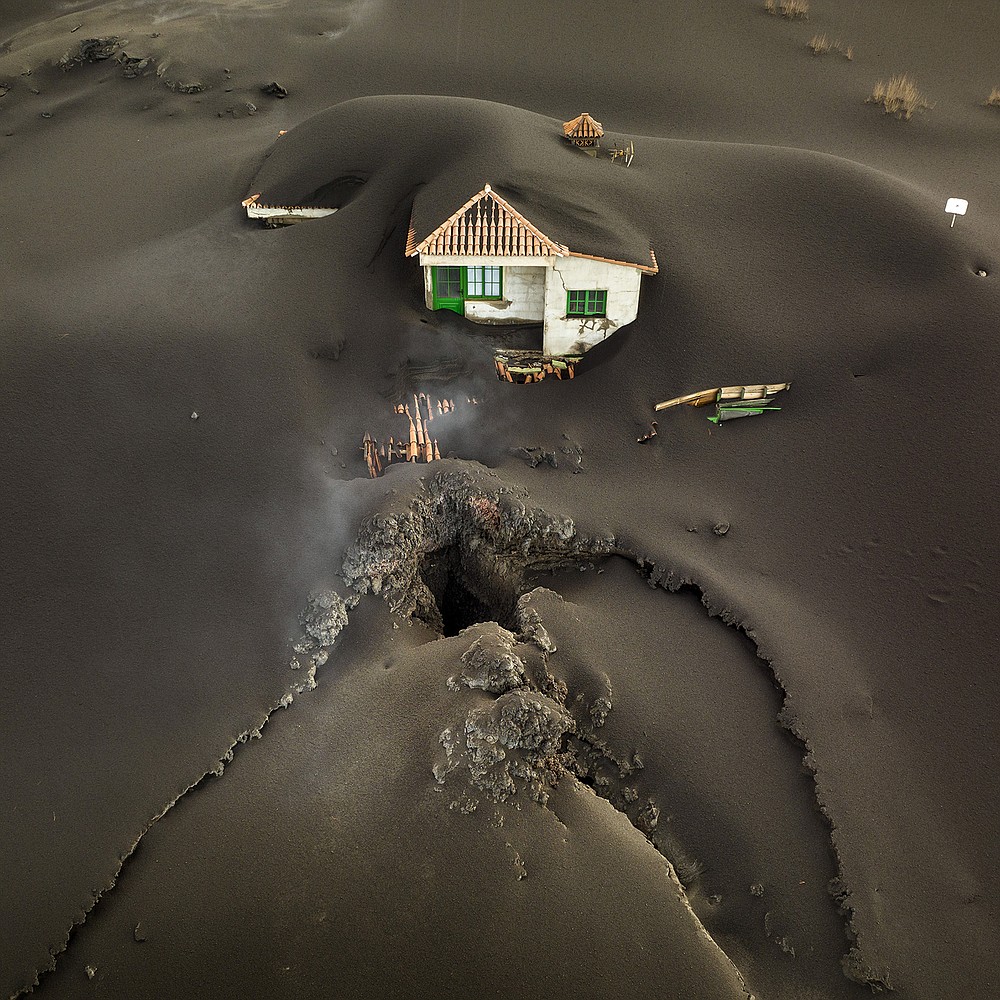 A fissure runs in front of a house covered with volcanic ash Wednesday on Spain’s island of La Palma. The fissure spouted a fresh gusher of lava that left a gaping hole in front of the house and threatened to engulf a parish church that has so far survived an eruption that has been going strong for 10 weeks.
(AP/Emilio Morenatti)