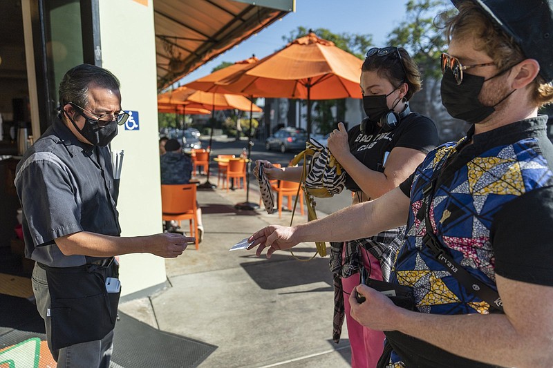 Waiter Juan Rodrigues (left) checks vaccination cards before patrons enter the Fred 62 restaurant in Los Angeles on Monday. Activity at restaurants and other service industries rose to a record in November.
(AP/Damian Dovarganes)