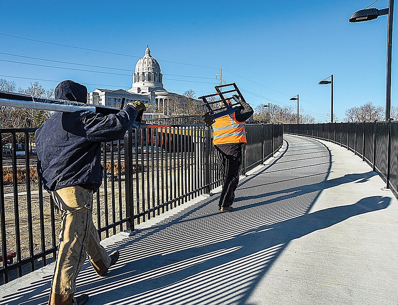 As crews from Stockman Construction and Phillips Hardy perform concrete work at the entrance to the Bicentennial Bridge, another crew from Collins & Hermann are busilly working to complete the installation of the fence that borders both sides of the pedestrian pathway. James K. Turpin, left, and Clint Dull of Collins & Hermann are shown carrying sections of the fence up the bridge to the safety enclosure.