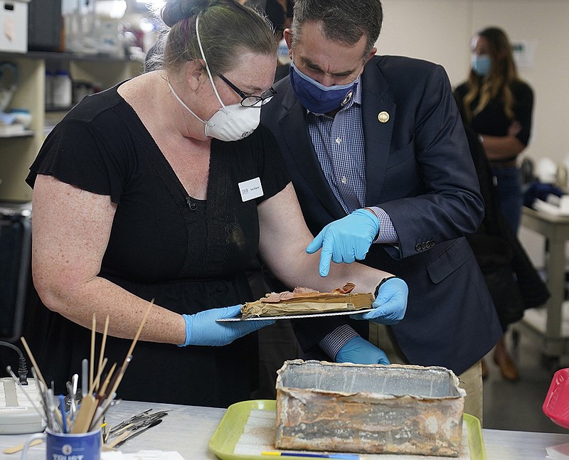 Kate Ridgway, lead conservator for the Virginia Department of Historic Resources, and Virginia Gov. Ralph Northam inspect a book Wednesday that was removed from a 130-year-old time capsule under the statue of Confederate Gen. Robert E. Lee after the statue was taken down in Richmond, Va. Three books and a cloth envelope with a photo were inside the box.
(AP/Steve Helber)