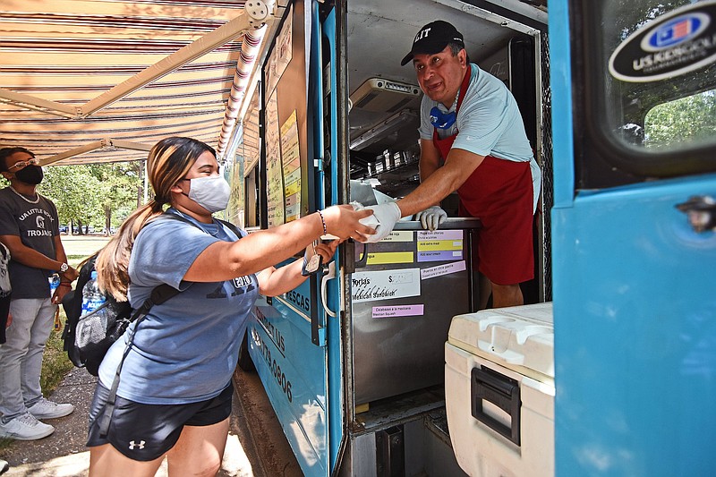 Tacos Godoy owner-operator Alejandro Gutierrez hands lunch to a University of Arkansas at Little Rock student. (Democrat-Gazette file photo/Staci Vandagriff)