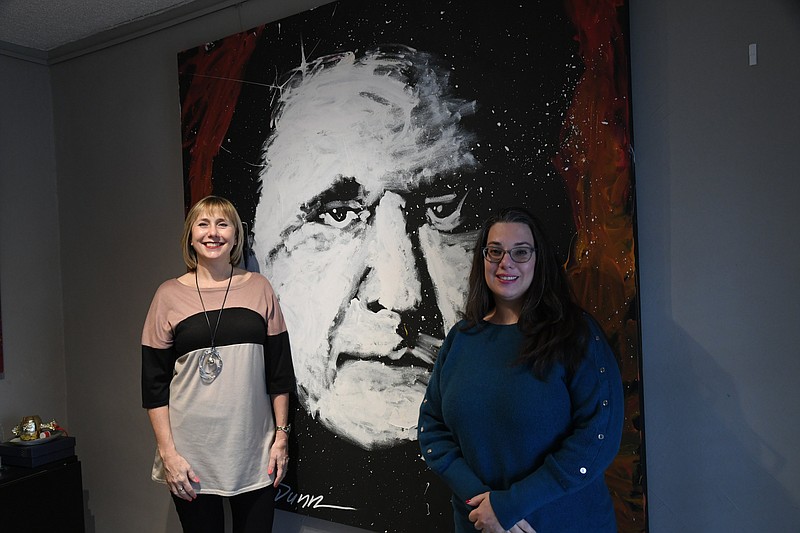 Mary Zunick, left, and Liz Colgrove stand next to a painting of Johnny Cash that was created during an earlier Arts & The Park festival. The two are currently planning this year’s festival. - Photo by Tanner Newton of The Sentinel-Record