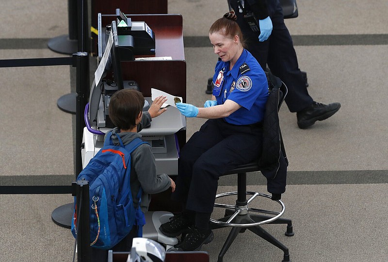 A Transportation Safety Administration agent hands a boarding pass to a young passenger at the south security checkpoint in Denver International Airport in this April 1, 2020, file photo. (AP/David Zalubowski)