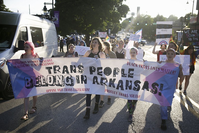 Attendees hold up banners and signs during a trans rights march that started at the Walton Arts Center and ended at the Town Center Plaza in downtown Fayetteville in this June 24, 2021, file photo. (NWA Democrat-Gazette/Charlie Kaijo)