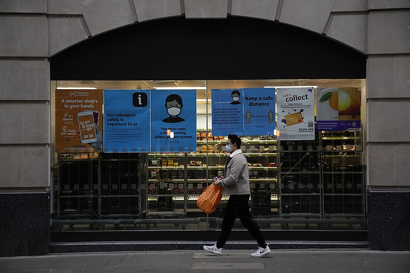 A shopper passes face covering signs displayed in the window of a Sainsbury’s supermarket store Thursday in London. The signs no longer apply under new guidelines.
(AP Photo/Matt Dunham)