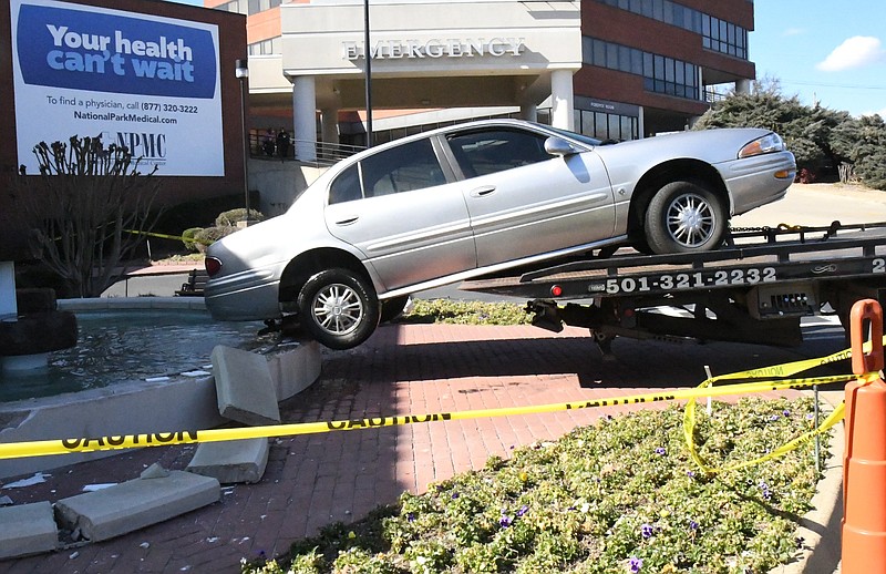 Employees of Burks & Mahoney Wrecker Service work to remove a vehicle that struck the fountain near the front entrance to National Park Medical Center on Tuesday. - Photo by Tanner Newton of The Sentinel-Record