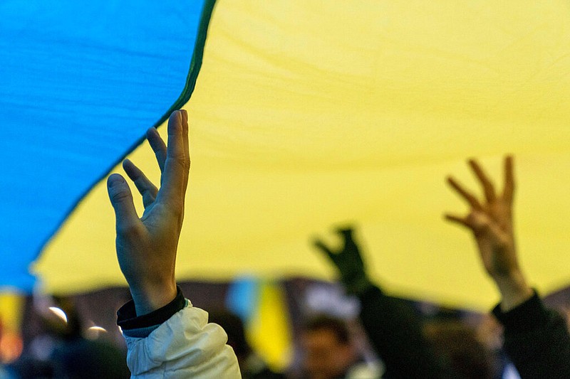 People stand under a giant Ukrainian flag during a vigil to protest the Russian invasion of Ukraine in front of the White House in Washington, Thursday, Feb. 24, 2022. (AP Photo/Andrew Harnik)