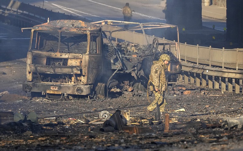 A Ukrainian soldier walks past the debris of a burning military truck on a street in Kyiv, Ukraine, on Saturday, Feb. 26, 2022. Russian troops stormed toward Ukraine's capital Saturday, and street fighting broke out as city officials urged residents to take shelter. (AP/Efrem Lukatsky)