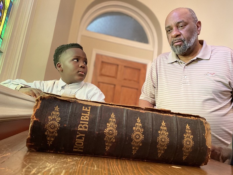 As Christopher Wilson, 7, looks on, Paul Williams, chairman of the board of deacons at First Missionary Baptist Church in Little Rock, discusses the congregation’s 19th-century Bible. Used by Martin Luther King Jr. when he preached at the church in 1963, a state grant will help pay for its restoration.(Arkansas Democrat-Gazette/Frank E. Lockwood)