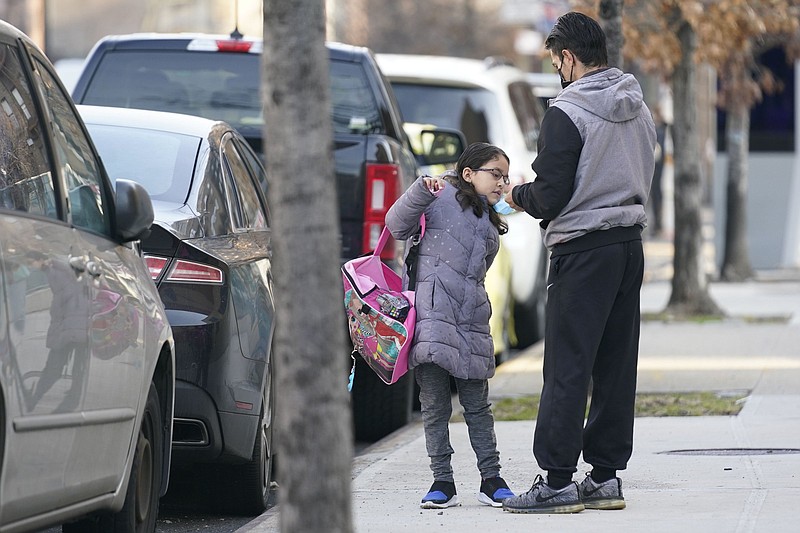 Paul Alban helps his daughter, second-grader Melanie Alban, adjust her mask before entering her school in New York, Monday, March 7, 2022. New York City passed a COVID-19 milestone on Monday as masks became optional in city schools and restaurants and other businesses could stop asking patrons for proof of vaccination. (AP Photo/Seth Wenig)