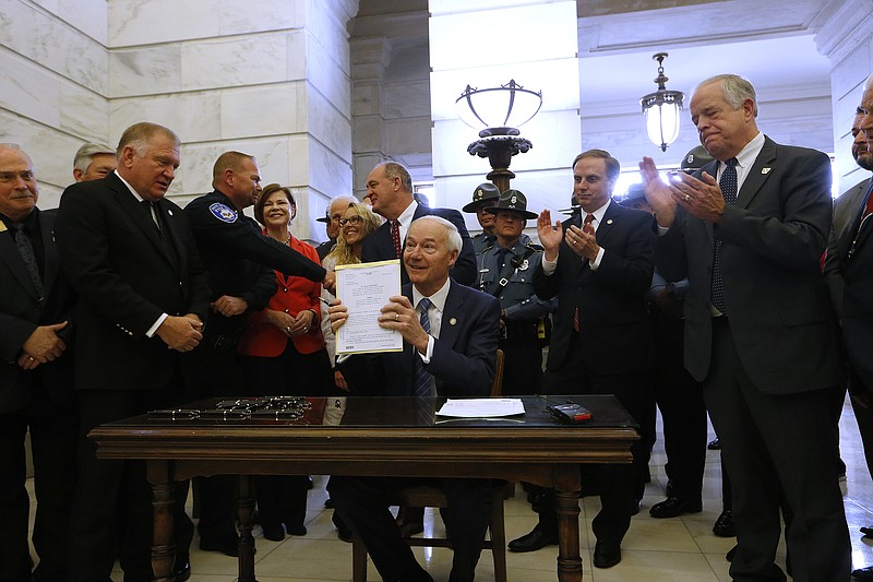 Gov. Asa Hutchinson holds up SB103 after signing the bill along with HB1026 during a bill signing ceremony in the state Capitol rotunda in Little Rock on Tuesday, March 8, 2022. The bills gave a one-time $5,000 stipend to full-time certified city and county law enforcement officers and full-time certified state Department of Corrections probation and parole officers and a raise to state troopers. The bill also gave troopers a one-time stipend of $2,000. (Arkansas Democrat-Gazette/Thomas Metthe)