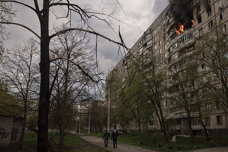 People walk near an apartment on fire after it was hit during a Russian bombardment in Kharkiv, Ukraine, Friday, April 22, 2022. (AP/Felipe Dana)