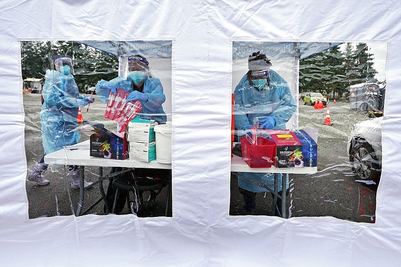 FILE - Workers at a drive-up covid-19 testing clinic stand in a tent as they prepare PCR coronavirus tests, Jan. 4, 2022, in Puyallup, Wash., south of Seattle. (AP/Ted S. Warren, File)