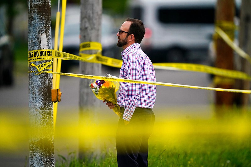 A person brings flowers to the perimeter of the scene of a shooting at a supermarket, in Buffalo, N.Y., Monday, May 16, 2022. (AP/Matt Rourke)