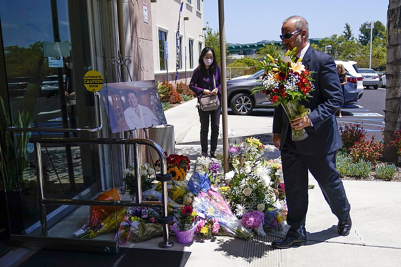 A man places flowers at a memorial honoring Dr. John Cheng sits outside his office building on Tuesday, May 17, 2022, in Aliso Viejo, Calif. Cheng, 52, was killed in Sunday's shooting at Geneva Presbyterian Church. (AP Photo/Ashley Landis)