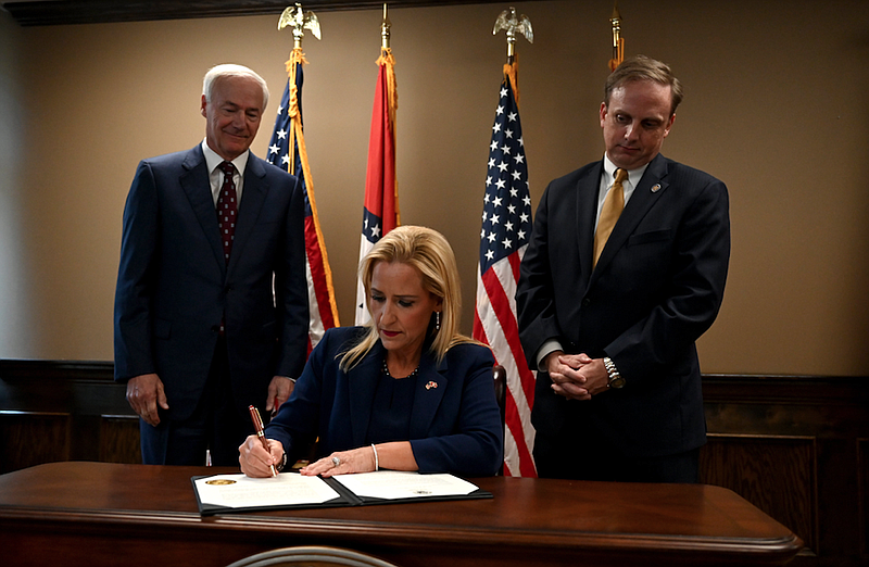 Governor Asa Hutchinson, left, and Matthew Shepherd, Speaker of the House, right, watch as Leslie Rutledge, Arkansas Attorney General, signs the official certification to prohibit abortions in Arkansas during a press conference in Little Rock on Friday, June 24, 2022. (Arkansas Democrat-Gazette/Stephen Swofford)