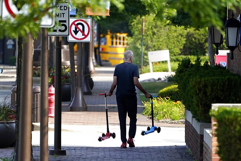 A man removes two children's scooters one day after a mass shooting in downtown Highland Park, Ill., Tuesday, July 5, 2022. (AP/Charles Rex Arbogast)