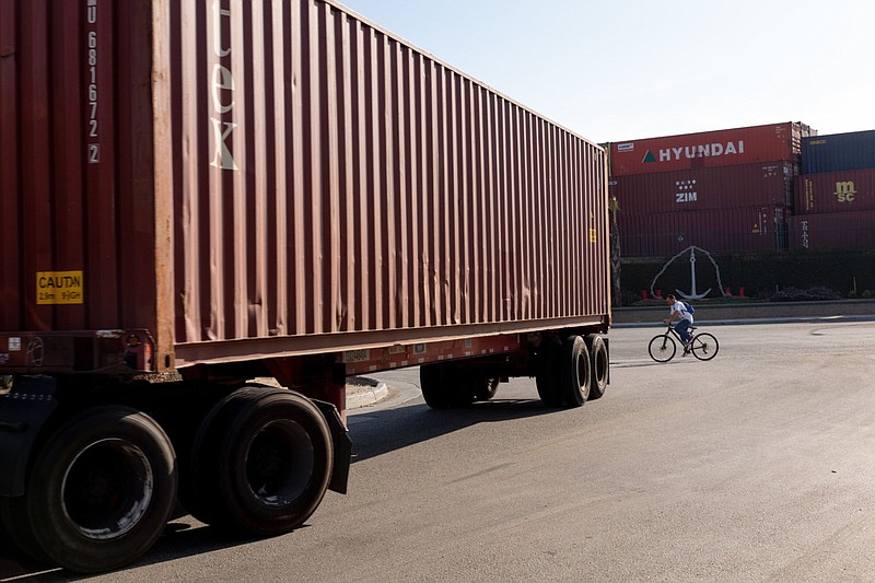 A truck hauling a shipping container passes a bicyclist on a street in the Wilmington neighborhood of Los Angeles. California’s independent truckers now face compliance with state law that requires them to satisfy a three-part test to be considered independent contractors.
(Bloomberg News WPNS/Allison Zaucha)