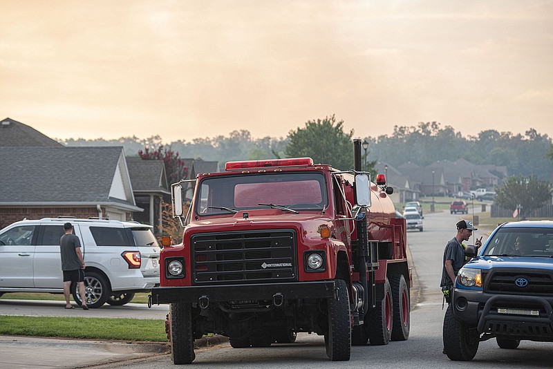 The driver of a Greenwood Rural Fire Department tanker speaks with residents along Maple Ridge Drive as smoke rises behind them on Tuesday, July 12, 2022, in Greenwood. According to the Sebastian County Sheriff’s Office, a large grass fire breached a fire break at Fort Chaffee and began spreading toward the residential Hilltop Addition in Greenwood, requiring some evacuations before multiple emergency agencies helped contain it. Greenwood mayor Doug Kinslaw said it was reminiscent of a fire in the area in 2011 that consumed a house before responders could react to it, though he said this time the multiple agencies helped contain 90% of the fire before any homes could be damaged. “Amazing response,” Kinslaw said. “And nobody was hurt. That’s the key.” Visit nwaonline.com/220713Daily/ for today's photo gallery..(NWA Democrat-Gazette/Hank Layton)