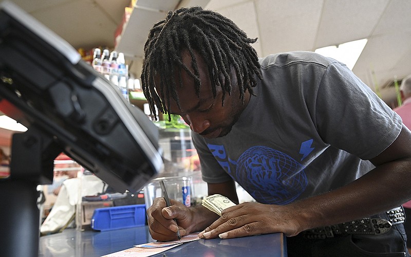 Michael Dawkins fills out a Mega Millions ticket he was buying for his mother Thursday at the Exxon station on University Avenue in Little Rock. “I don’t think there’s anybody that lucky, not in Arkansas” to win the huge jackpot, Dawkins said.
(Arkansas Democrat-Gazette/Stephen Swofford)