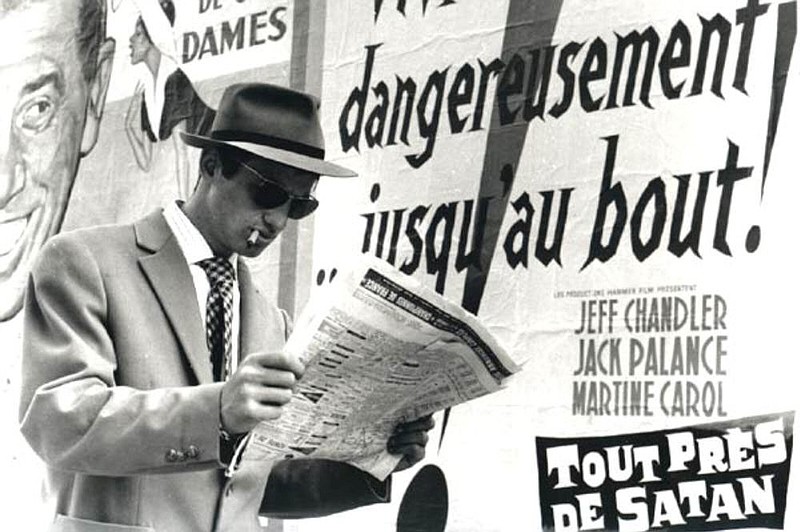 Young thug Michel (Jean-Paul Belmondo), who models himself on the screen persona of Humphrey Bogart, reads a newspaper in front of a poster for the Robert Aldrich movie “10 Seconds to Hell” in a scene from Jean-Luc Godard’s 1960 film “A Bout de Souffle” — better known to American audiences as “Breathless.”