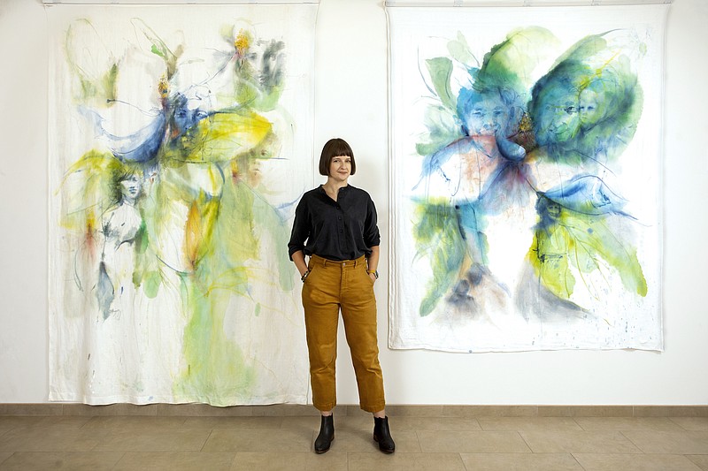 Artist Emily Wood shows off two of her flower studies painted on heirloom tablecloths at Thea Foundation in North Little Rock’s Argenta district. (Special to the Democrat-Gazette)