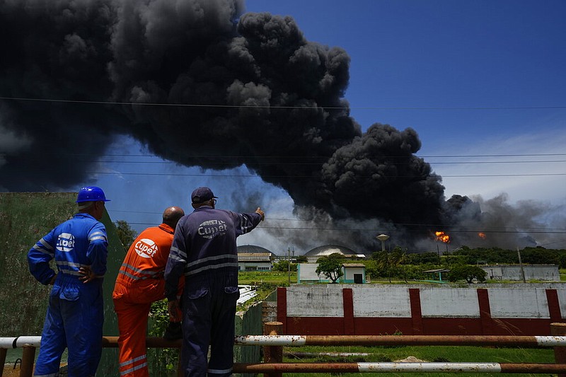 Workers of the Cuba Oil Union, known by the Spanish acronym CUPET, watch a huge rising plume of smoke from the Matanzas Supertanker Base, as firefighters work to quell a blaze which began during a thunderstorm the night before, in Matazanas, Cuba, Saturday, Aug. 6, 2022. (AP/Ramon Espinosa)