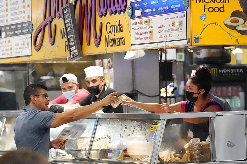 Money is exchanged at a food stand while workers wear face masks inside Grand Central Market on Wednesday, July 13, 2022, in Los Angeles. (AP/Marcio Jose Sanchez)