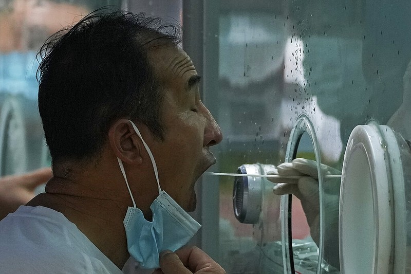 A man pulls his mask to get his routine covid-19 throat swab at a coronavirus testing site in Beijing, Tuesday, Aug. 9, 2022. (AP Photo/Andy Wong)