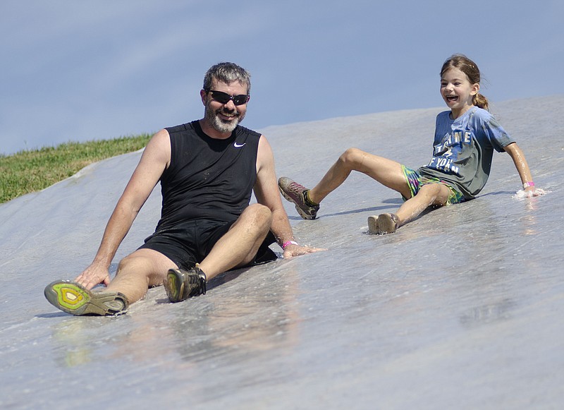Derek, left, and Piper Redel, 8, slide down a slip n' slide on Saturday, August 27, 2022, at Ellis-Porter Riverside Park in Jefferson City. The father and daughter duo completed the obstacle course and Piper said her favorite part was the mud pit. (Eileen Wisniowicz/News Tribune photo)
